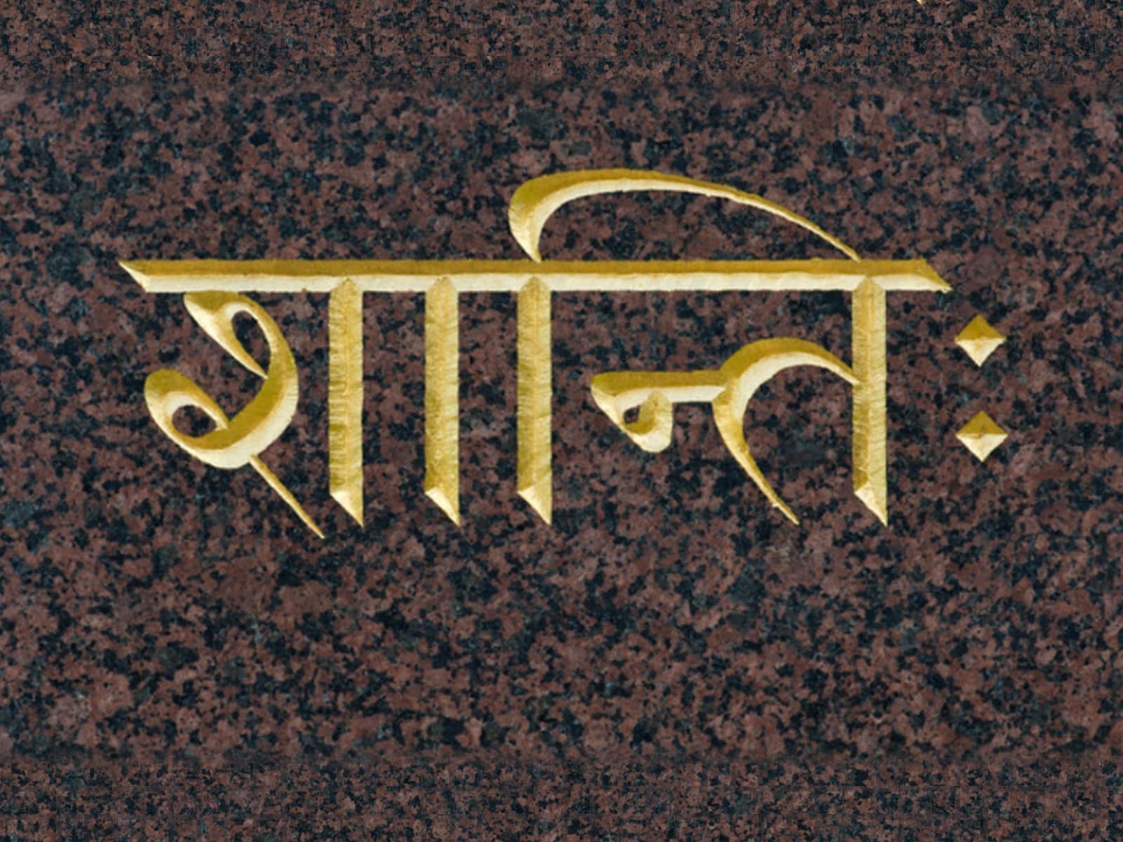 The Sanskrit word shanti, peace, in gold Devanagari letters on dark stone