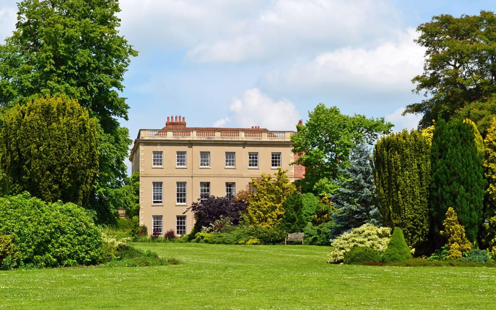 Waterperry House, Oxfordshire (the Jacobean stone facade seen across the lawn in spring, lilac wisteria across the front elevation)
