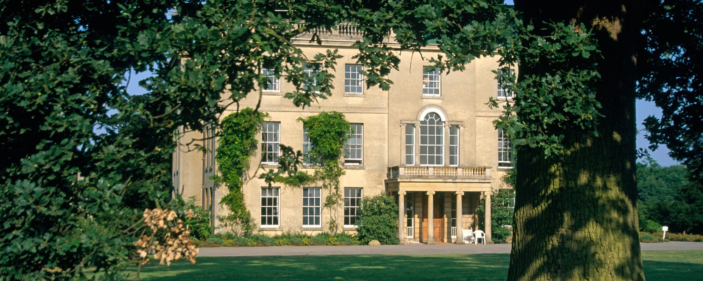 Waterperry House portico and facade framed by mature trees across a green lawn