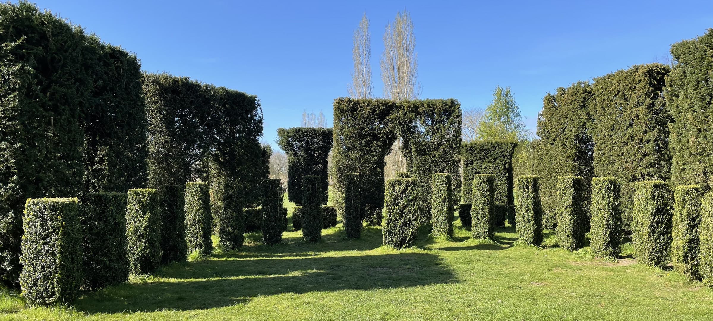 Yew pillars and a hedge doorway framing tall trees in the Waterperry gardens
