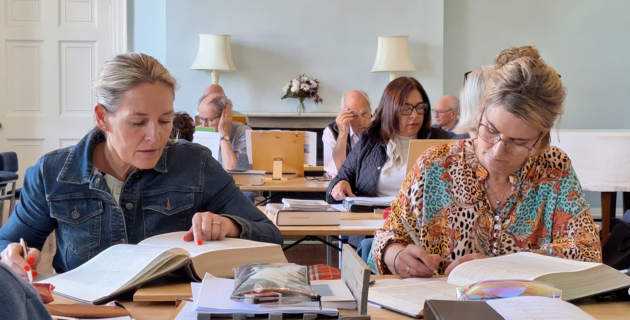 Adults studying thick open books at wooden desks in a bright, quiet room