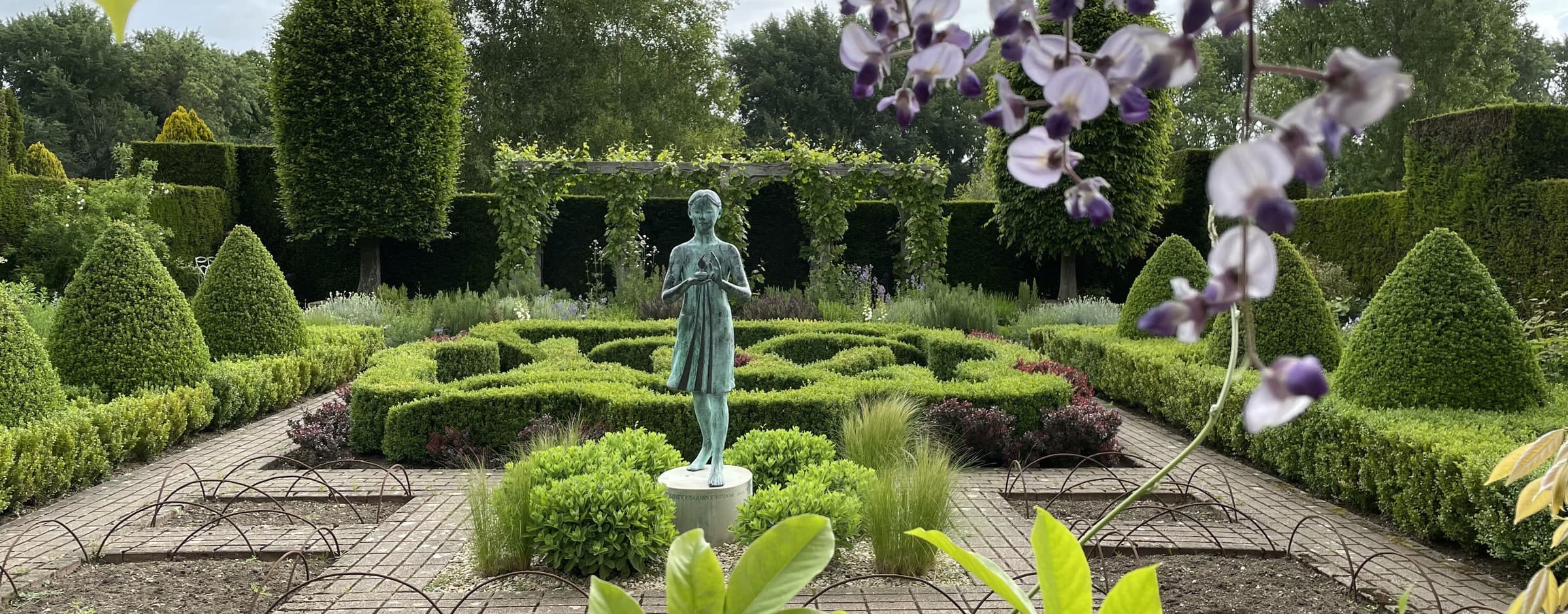 Bronze statue in a knot garden with conical topiary at Waterperry